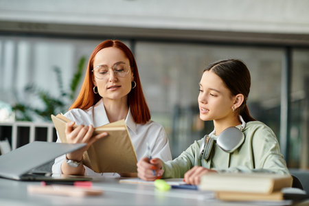 Redhead woman tutors teenage girl at a table with a book, engaging in after-school lessons, enhancing modern education.の写真素材