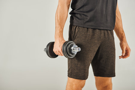A young sportsman in active wear energetically lifts a pair of dumbbells in a studio with a grey background.の写真素材