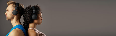 A young multicultural couple in active wear listening to music through headphones on a gray background in a studio.の写真素材