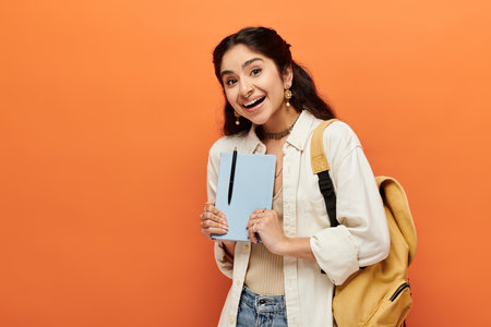 Young indian woman confidently holds notebook on orange background.の写真素材