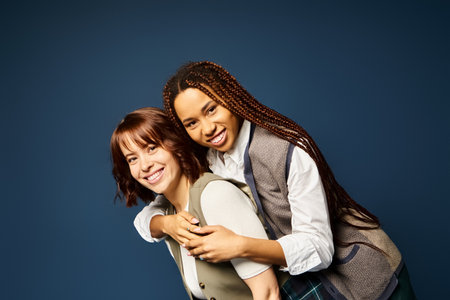 Two young women, hugging joyfully in stylish attire against a dark blue background.の写真素材