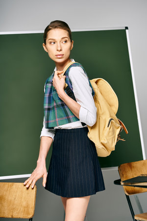 Female student in skirt and backpack stands before chalkboard.の写真素材
