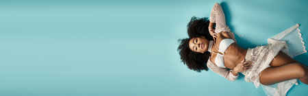 Young African American woman relaxing in stylish bikini on serene blue backdrop.の写真素材