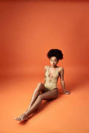 Stylish woman in swimsuit relaxing on orange backdrop.の写真素材