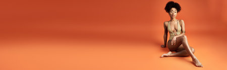 Young African American woman sitting gracefully on orange backgroundの写真素材