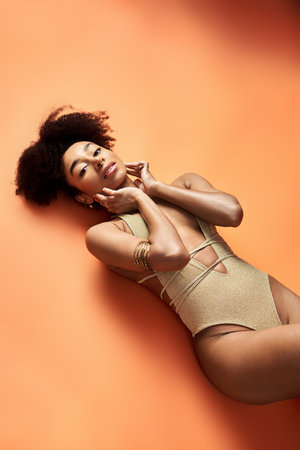 Stylish African American woman sunbathing in trendy swimsuit on bright orange background.の写真素材