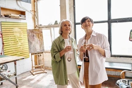 Two mature women, a loving couple, stand side by side in an art studio.の写真素材