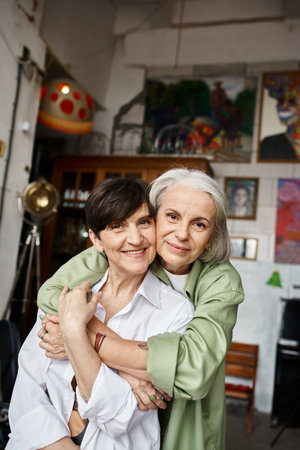 Two mature women hug each other in a cozy art studio.の写真素材