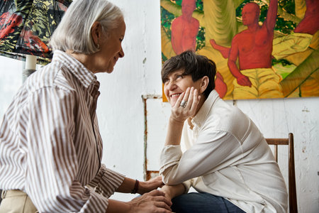 Two women sit together in an art studio, working on a project.