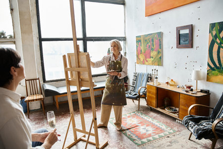 Woman standing at easel holding wine glass, painting partner.の写真素材
