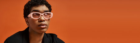 Handsome African American man in pink glasses against orange backdrop.の写真素材