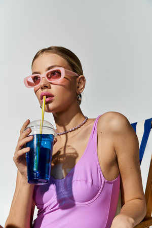 Trendy blonde woman in chic pink swimsuit enjoying a refreshing drink.の写真素材