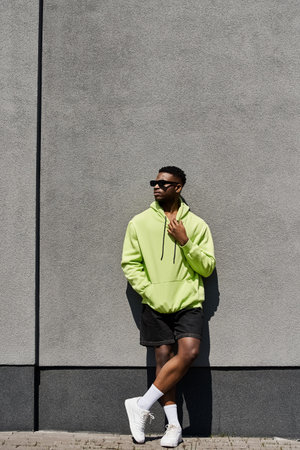 Stylish African American man in green hoodie leaning against a wall.の写真素材