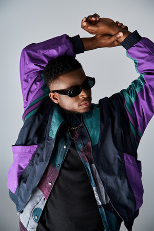 A fashionable young African American man in a purple jacket and sunglasses poses for the camera.