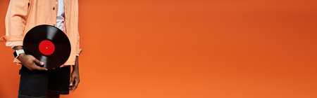 Stylish black man holding vinyl record against vibrant orange backdrop.