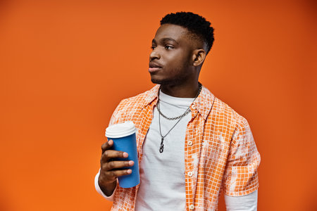 Handsome young man holds cup of coffee against bright orange backdrop.