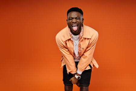 Stylish African American man sticking his tongue out against a bright orange backdrop.の写真素材