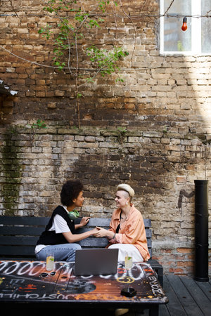 A diverse couple of lesbians engaged in conversation on a bench in a cafe.の写真素材