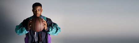 Handsome African American man showcasing trendy attire while holding a basketball.の写真素材