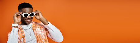 Fashionable young African American man in sunglasses on vivid orange background.