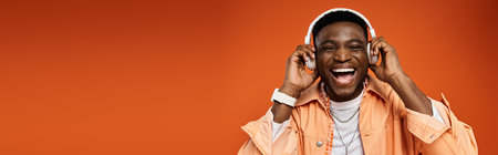 Stylish African American man in orange shirt enjoying music.の写真素材