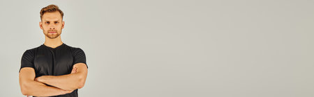 A muscular man showcases his strength with folded arms against a white backdrop.の写真素材