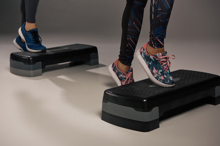 A young multicultural and fit couple in active wear, energetically standing on a pair of steppers in...