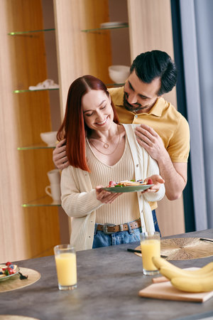 A beautiful adult couple, a redhead woman, and a bearded man, enjoying breakfast in a modern kitchen.の写真素材