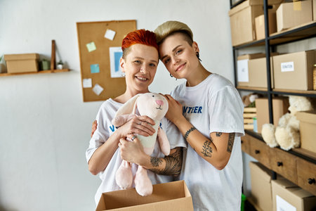 Young lesbian couple in volunteer t-shirts holding a stuffed animal, spreading joy during charity work.の写真素材