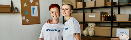 Two women, a young lesbian couple, wearing volunteer t-shirts, stand together with smiles, embodying unity and shared purpose.の写真素材