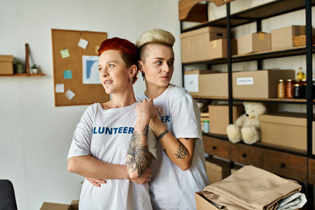 Two young women in volunteer t-shirts standing side by side, embodying unity and purpose in their charitable work.の写真素材