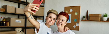 An enthusiastic woman happily takes a selfie with her friend, both wearing volunteer t-shirts.の写真素材