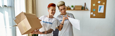 A young lesbian couple in volunteer t-shirts stand together, holding a box.の写真素材