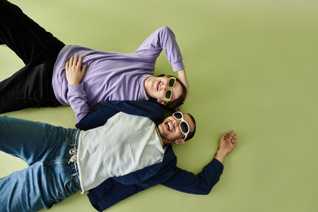 Two stylish men enjoying the sun, lounging on the ground in sunglasses.