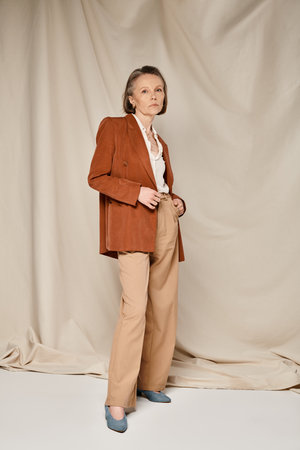 Stylish woman in tan blazer and pants, exuding confidence and sophistication while striking a pose.の写真素材