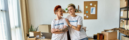 Two young women in volunteer t-shirts standing side by side in a room, united in their charitable work.の写真素材