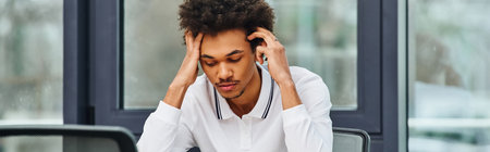 Man in distress sits at desk with head in hands.