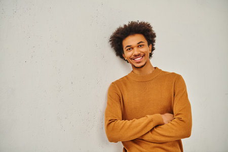 A stylish young man in a tan sweater leaning casually against a wall.の写真素材