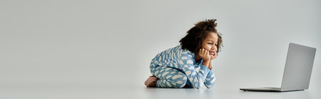 A little girl in pajamas mesmerized by a laptop while sitting on the floorの写真素材