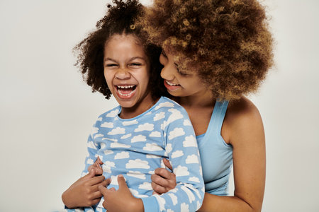 Happy African American mother and daughter in pajamas sharing a joyful moment, laughing together on a white background.の写真素材