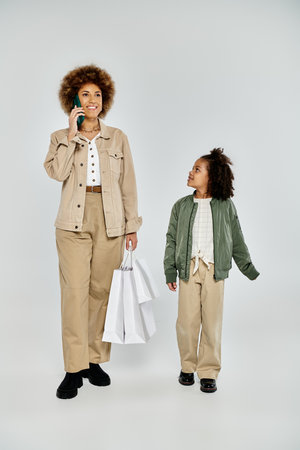 A curly African American mother and daughter, dressed stylishly, stand next to each other with...