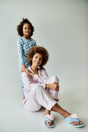 A cheerful African American mother and daughter in matching pajamas strike a pose on a grey background.の写真素材