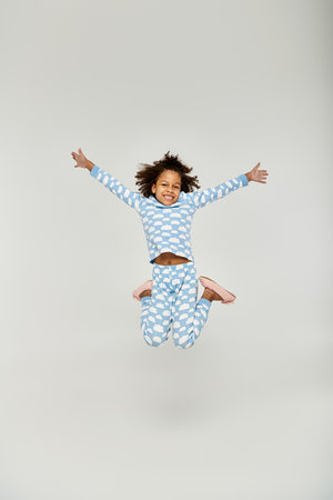 A young African American girl joyfully jumping in the air, wearing blue pajamasの写真素材