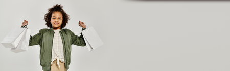 A young boy confidently holds shopping bags in front of a white background.の写真素材