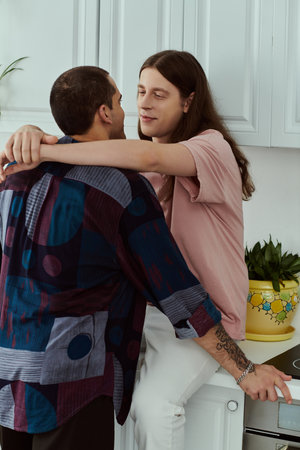 A gay couple in casual clothes embrace lovingly in a cozy kitchen, enjoying a tender moment...