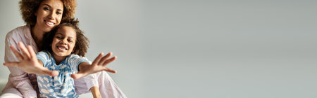 An upbeat African American mother and daughter, both in pajamas, strike a pose together on a grey background.の写真素材