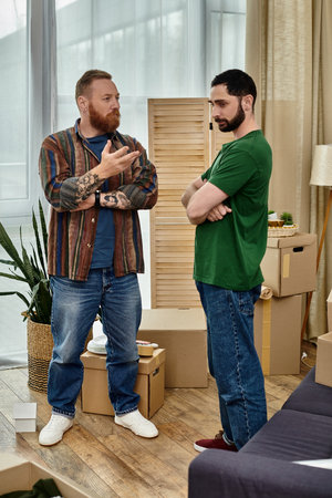 A gay couple in love stands in their new living room, surrounded by moving boxes, having...
