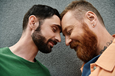 A gay couple in love, dressed in casual attire, standing closely together against a gray wall.の写真素材