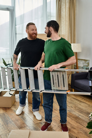 Two men, a gay couple, stand together in their living room and holding ladder, beginning a new...