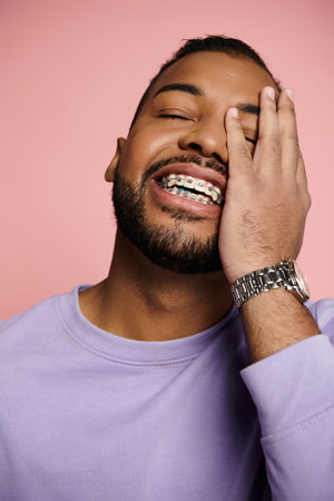A young African American man smiling brightly, showcasing his braces, against a vibrant pink...